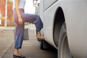 A woman in denim capri pants with black and white shoes stepping onto a bus